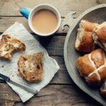 mug of tea and plate of hot cross buns with one split and buttered 
