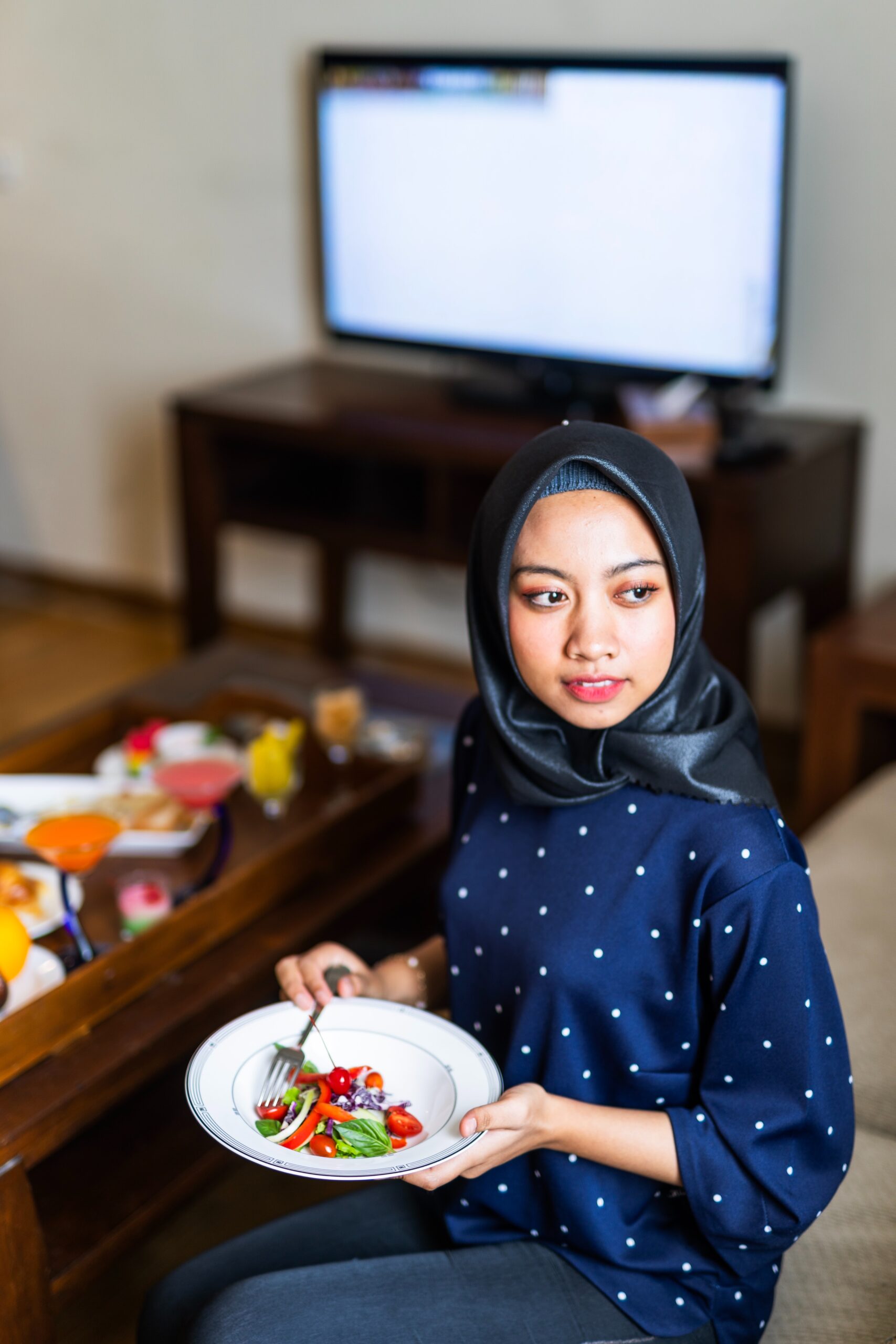 woman wearing hijab eating with tv on