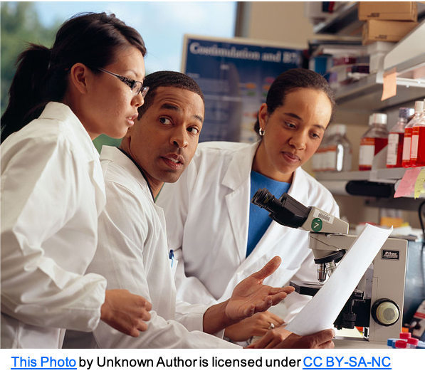 three adults in white coats in a lab