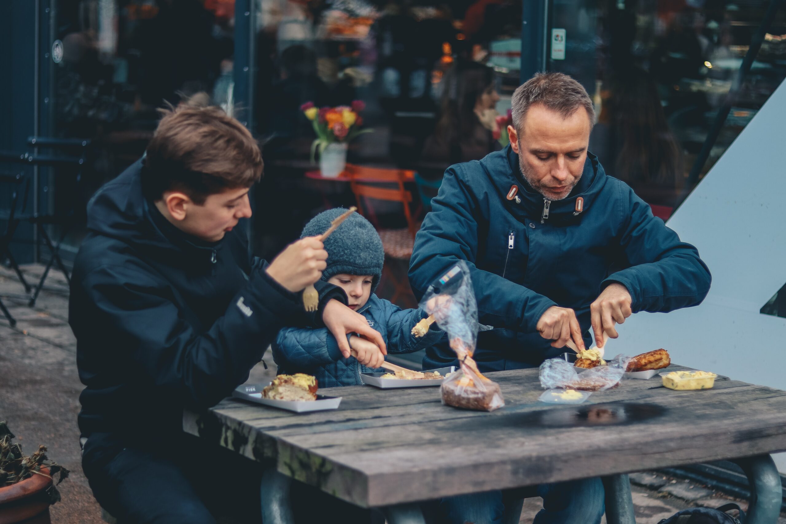 Two people sat at picnic bench helping young child cut up food