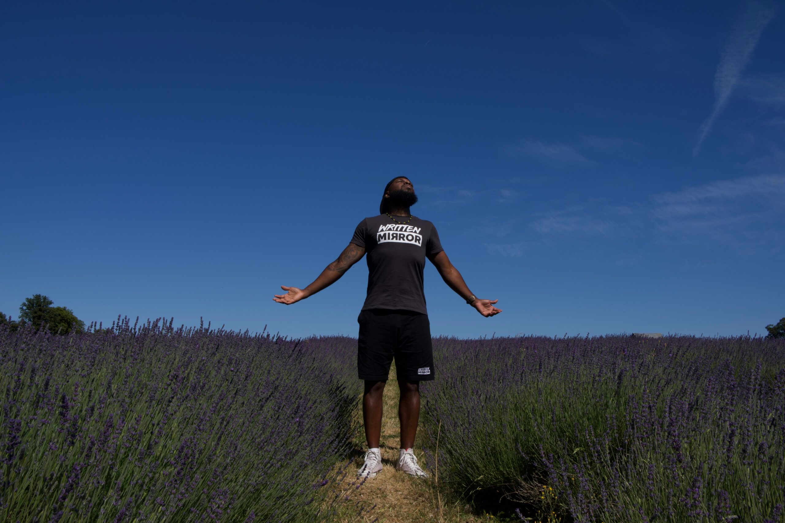 man in shorts and T shirt with arms outstretched and face turned up to sun