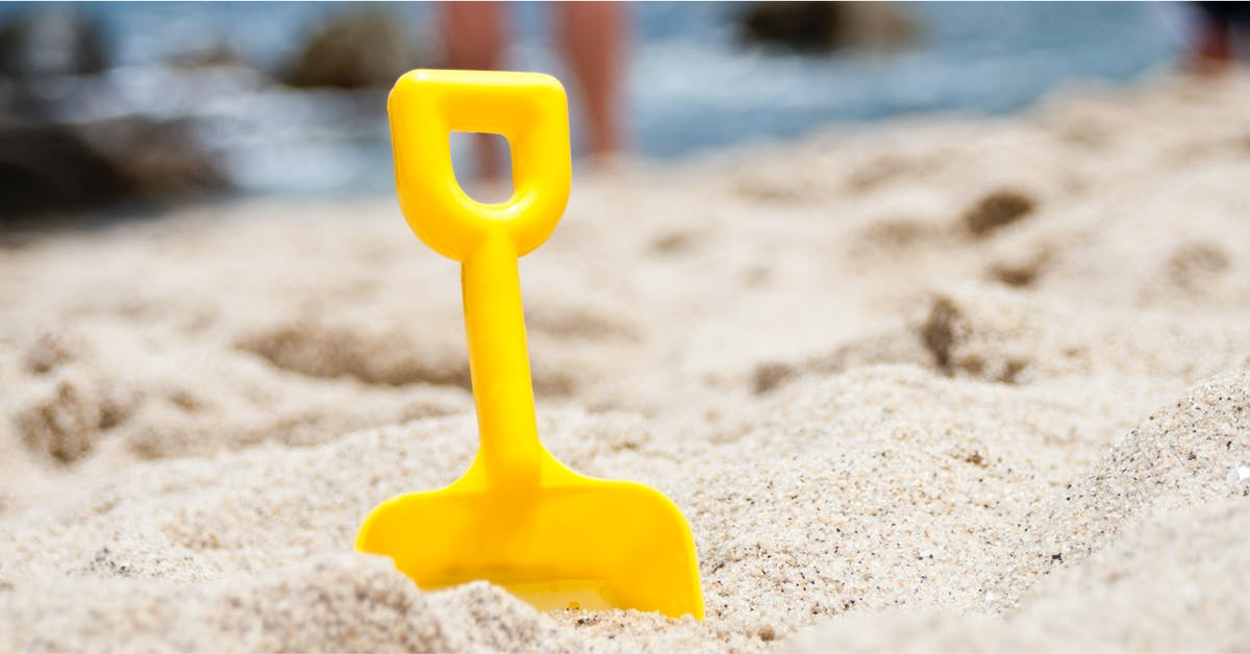 child's yellow plastic spade in sand