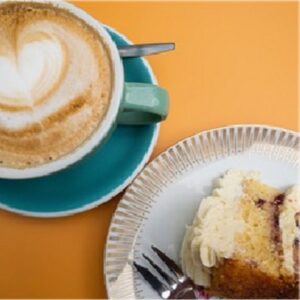 photo of milky drink in teal cup and saucer and iced cake and fork on a white plate